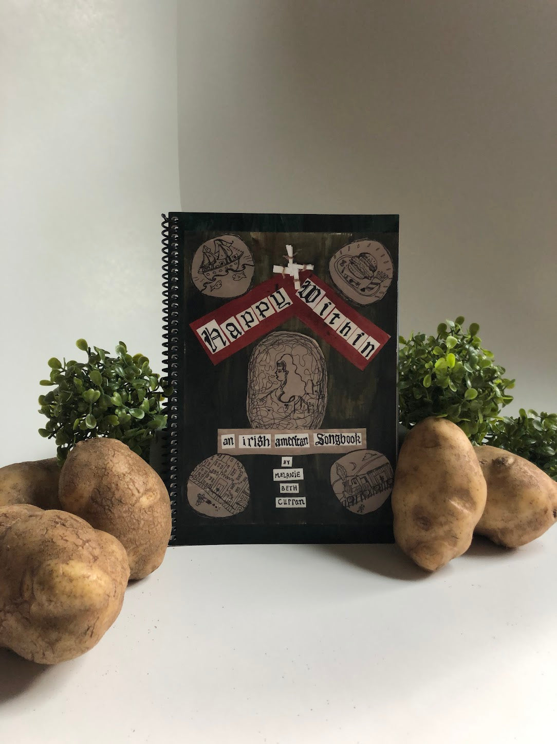 Irish American Song Book with a decorative handmade  cover surrounded by potatoes on a white surface
